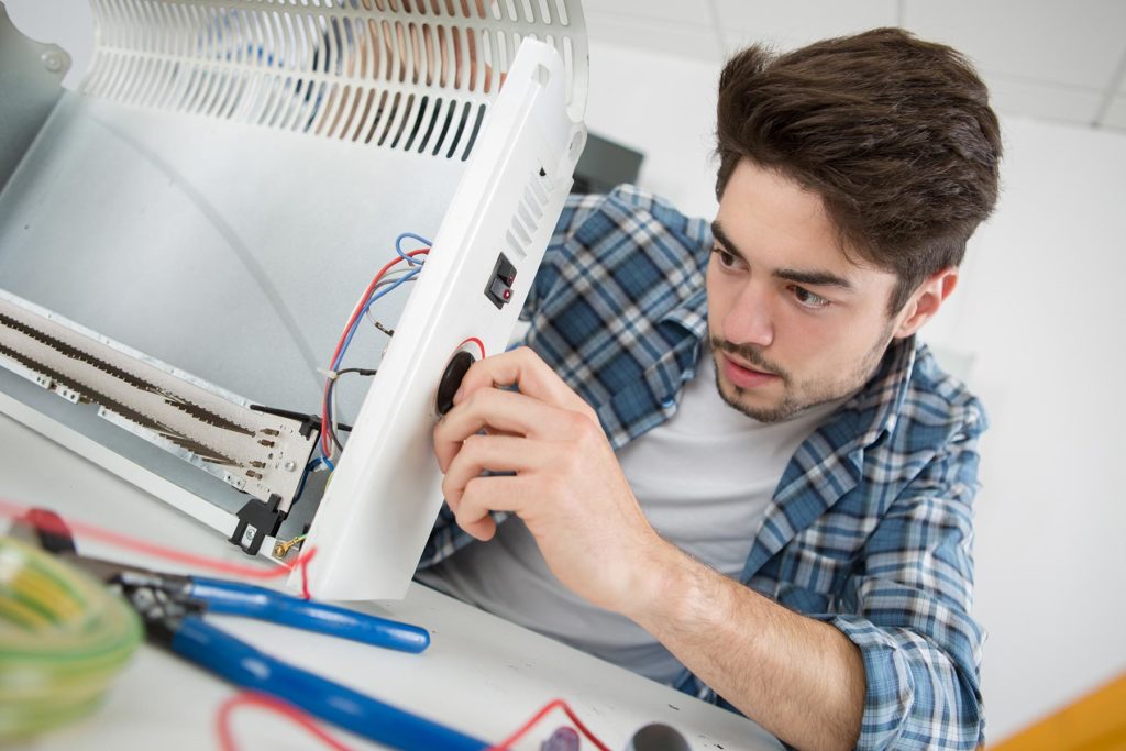 young-male-plumber-examining-electric-heater-PLXD3ZH.jpg